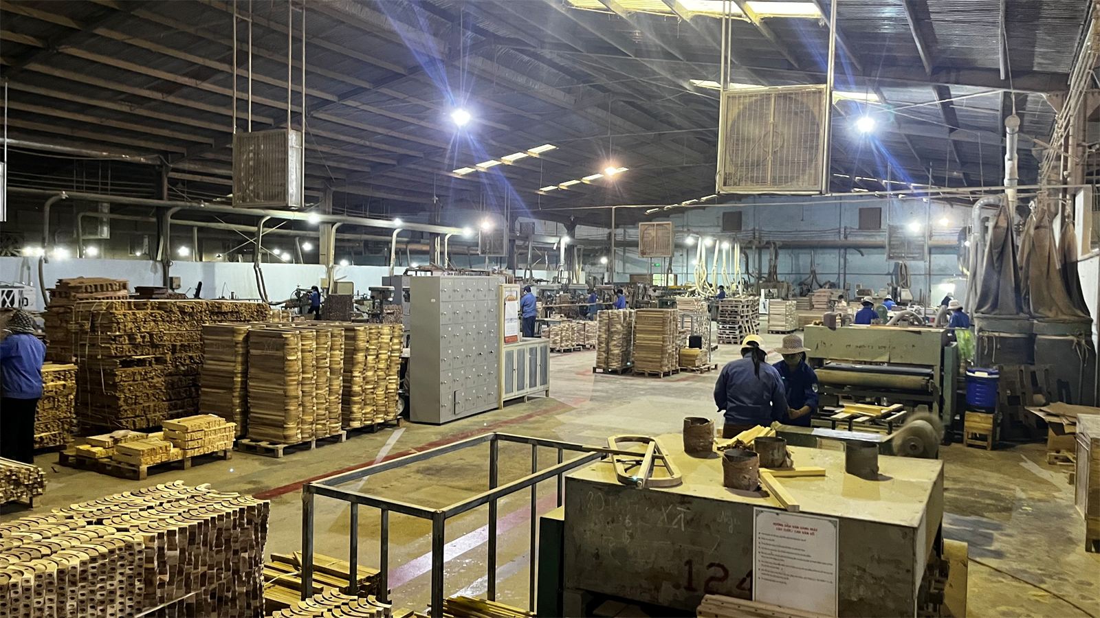 Factory hall with stacks of wooden parts on pallets and manual handling
